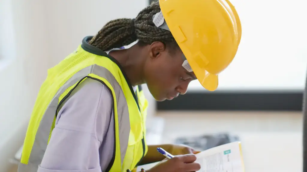An inspector in a hard hat and hi-vis vest making notes on a clipboard