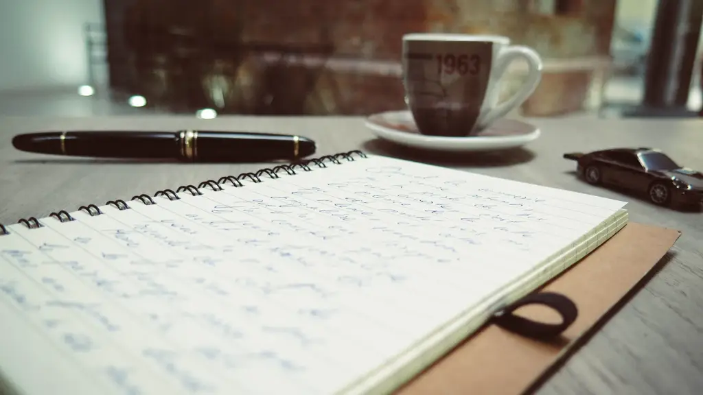 An open notebook and pen beside a cup of coffee